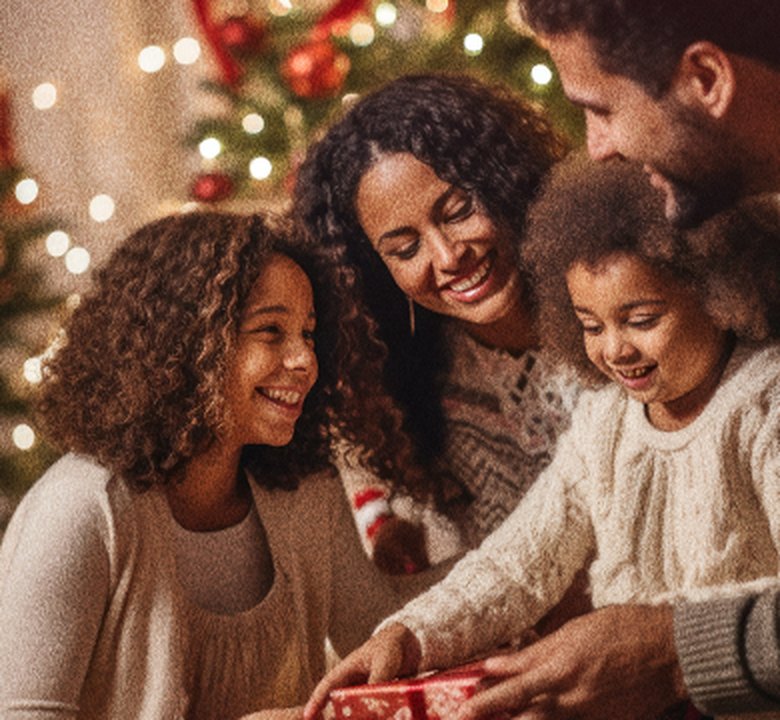 Família sorrindo ao abrir um presente diante da árvore de Natal